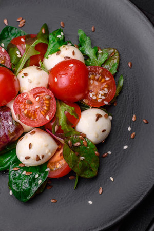 Delicious fresh salad with mozzarella cheese, cherry tomatoes, herbs, salt and spices on a dark concrete backgroundの写真素材