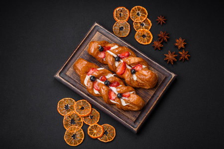 Delicious fresh crispy pastry in the form of a pigtail with strawberries and blueberries on a dark...