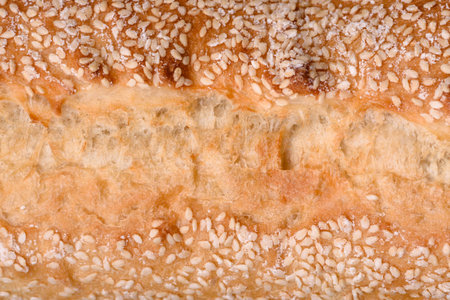 Crispy wheat flour baguette with sesame seeds on a wooden cutting board on a dark concrete...