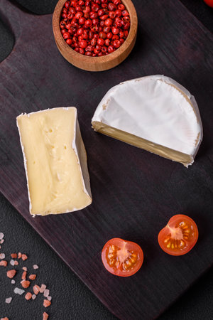Delicious fresh brie cheese in the form of a mini head with cherry tomatoes on a dark concrete...