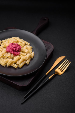 Delicious fusilli pasta with beetroot pesto, parmesan, salt and spices on a dark concrete backgroundの写真素材