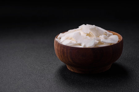 White dry coconut flakes in a wooden bowl prepared for making desserts on a textured concrete...