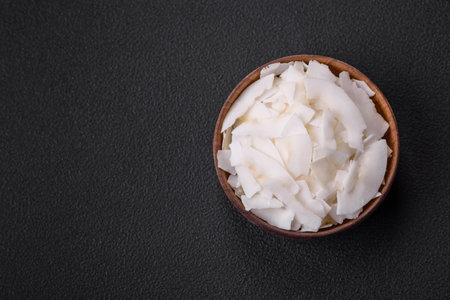 White dry coconut flakes in a wooden bowl prepared for making desserts on a textured concrete backgroundの写真素材