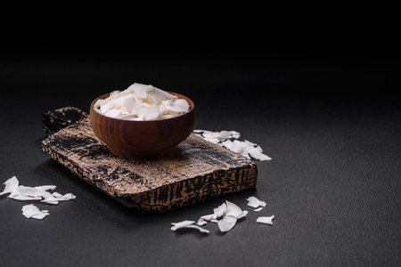 White dry coconut flakes in a wooden bowl prepared for making desserts on a textured concrete...