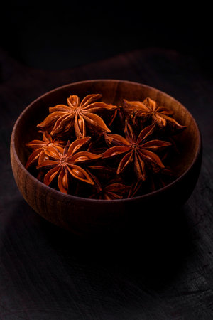 Star shaped spice star anise in a wooden round bowl on a dark concrete backgroundの写真素材
