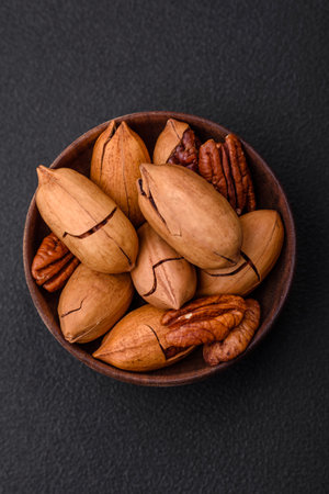 Pecan nuts in shell and peeled in a wooden round bowl on a dark concrete background