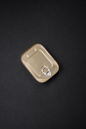 Tin or aluminum rectangular can of canned food with a key on a dark concrete background