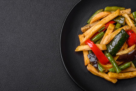 Delicious fried potatoes with bell peppers, asparagus beans, salt and spices in a plate on a dark...