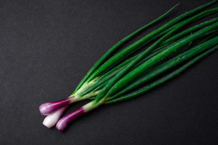 Fresh green onions for cooking a healthy vegetarian dish on a dark concrete backgroundの写真素材