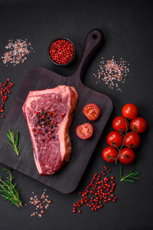 Fresh juicy raw new york beef steak with salt, spices and herbs on dark concrete backgroundの写真素材