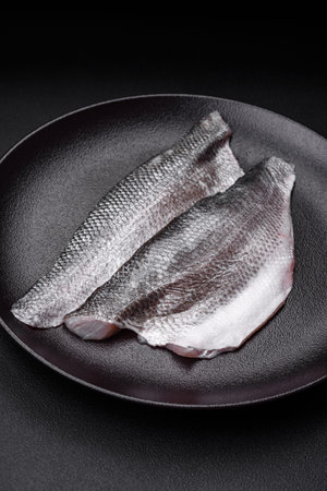 Raw sea bass fish fillet with salt, spices and herbs on a ceramic plate prepared for baking