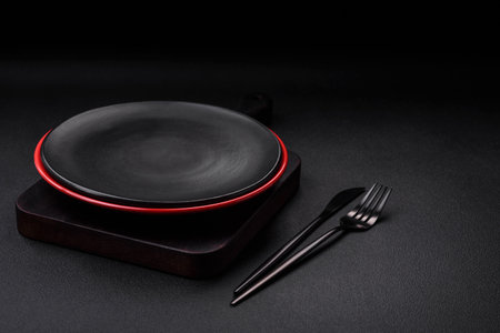 Empty ceramic plate on dark textured concrete background. Cutlery on the kitchen tableの写真素材