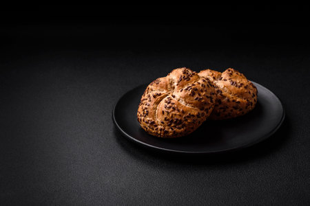 Delicious freshly baked crispy bun or kaiser roll with sesame seeds on dark concrete background