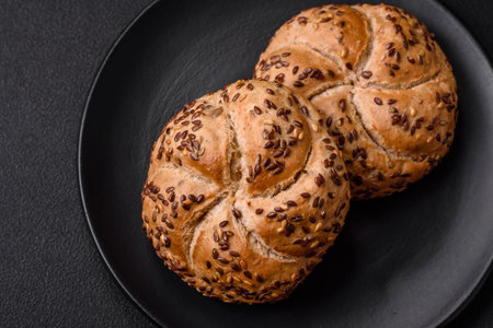 Delicious freshly baked crispy bun or kaiser roll with sesame seeds on dark concrete background