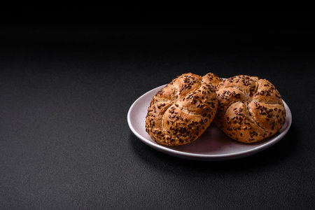 Delicious freshly baked crispy bun or kaiser roll with sesame seeds on dark concrete backgroundの写真素材