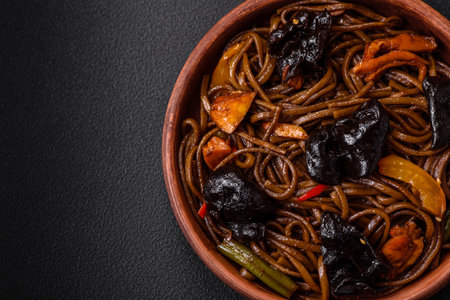 Delicious fresh buckwheat noodles or udon with mushrooms, peppers and other vegetables, spices and herbs on a dark concrete backgroundの写真素材