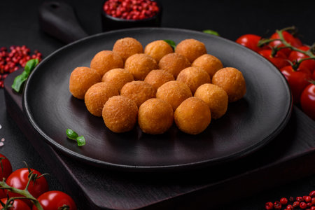 Delicious fried potato balls with breaded mozzarella, salt, spices and herbs on a dark concrete...