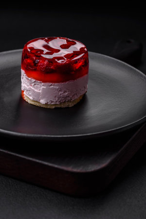 Delicious fresh sweet cheesecake cake with berries and red color jelly on a dark concrete backgroundの写真素材