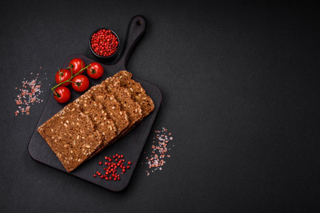 Delicious fresh crispy brown bread with seeds and grains cut into slices on a dark concrete...