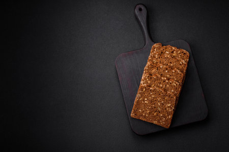 Delicious fresh crispy brown bread with seeds and grains cut into slices on a dark concrete...