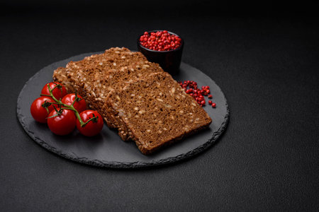 Delicious fresh crispy brown bread with seeds and grains cut into slices on a dark concrete backgroundの写真素材