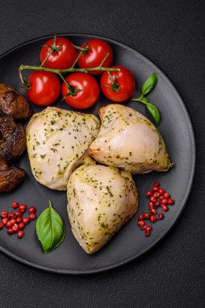 Delicious juicy grilled chicken with salt, spices and herbs with vegetables on a dark concrete backgroundの写真素材