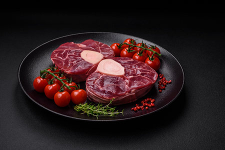Fresh raw beef steak with bone or ossobuco with salt, spices and herbs on dark concrete backgroundの写真素材