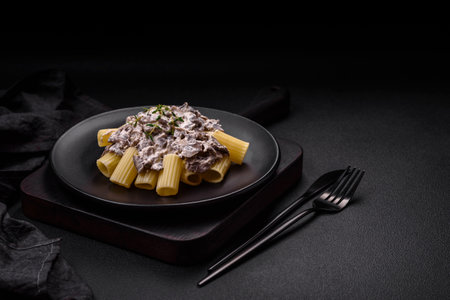 Delicious fresh pasta with champignon mushrooms in a creamy sauce with salt, spices and herbs on a dark concrete backgroundの写真素材