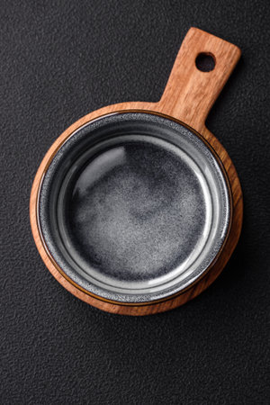 Empty round ceramic bowl on a wooden cutting board in brown color on a dark textured concrete backgroundの写真素材