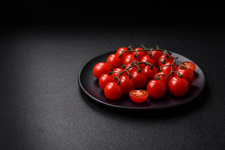 Delicious fresh cherry tomatoes on the branches as an ingredient for cooking a vegetarian dish on a dark concrete backgroundの写真素材