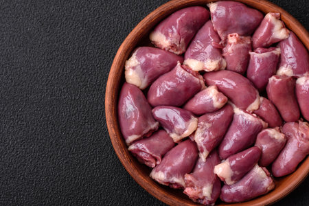 Fresh raw chicken or turkey hearts in a ceramic plate with salt, spices and herbs on a dark concrete backgroundの写真素材