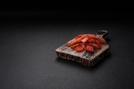 Delicious dried veal or turkey jerky with salt, spices and herbs on a dark concrete background