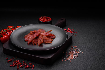 Delicious dried veal or turkey jerky with salt, spices and herbs on a dark concrete backgroundの写真素材
