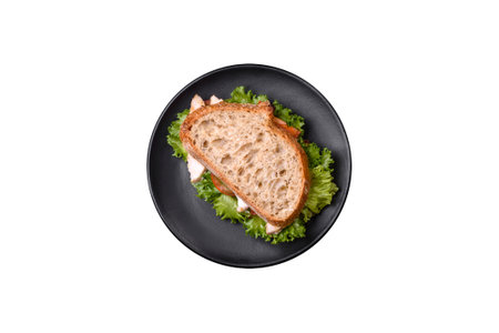 Fresh tasty sandwich with chicken, tomatoes and lettuce on a black plate on a dark concrete backgroundの写真素材