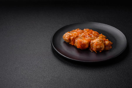 Delicious fresh sea fish cut into pieces and baked in tomato sauce with salt, spices and herbs on a dark concrete backgroundの写真素材