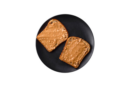 Nutritious sandwich consisting of bread and peanut butter on a black ceramic plate on a dark concrete backgroundの写真素材