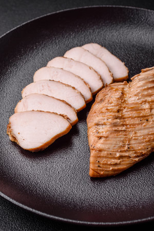 Delicious juicy grilled chicken fillet with salt, spices and herbs on a dark concrete backgroundの写真素材