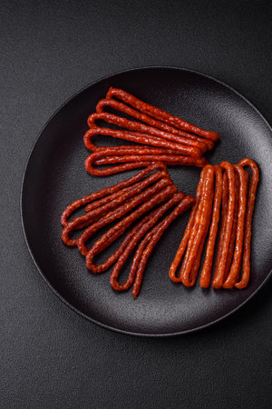 Delicious thin smoked hunting sausages with salt, spices and herbs on a dark concrete background
