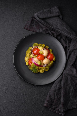 Delicious fresh salad with broccoli, cherry tomatoes, mushrooms, onions, salt, spices and herbs on a dark concrete backgroundの写真素材