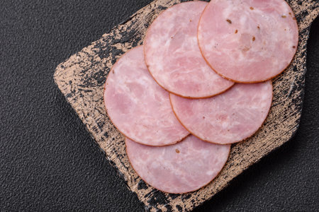 Delicious fresh ham cut into round slices with salt, spices and herbs on a dark concrete backgroundの写真素材