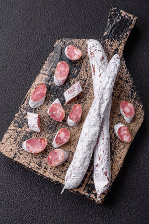 Delicious Spanish smoked sausage fuet with salt and spices on a dark concrete background