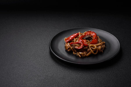 Delicious asian udon dish with vegetables, mushrooms, salt and spices on a ceramic plate on a dark concrete backgroundの写真素材