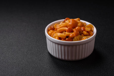 Delicious pickled honey mushrooms with salt and spices in a ceramic plate on a dark textured...