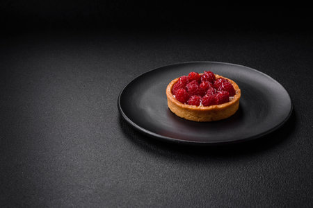 Delicious fresh sweet round tart with ripe raspberries and cream on a dark concrete backgroundの写真素材