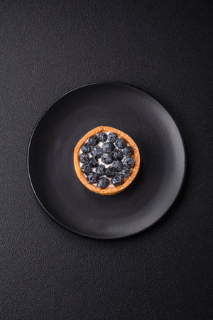 Delicious fresh sweet round tart with ripe blueberries and cream on a dark concrete backgroundの写真素材