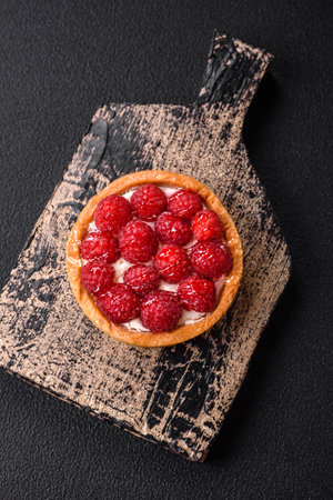 Delicious fresh sweet round tart with ripe raspberries and cream on a dark concrete backgroundの写真素材