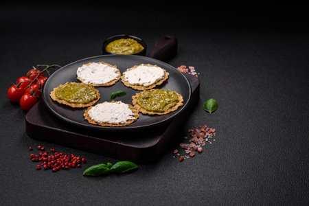 Round snacks with crispy chips or crackers with cream cheese and pesto on a ceramic plate
