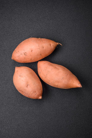 Fresh large pink sweet potato tubers with tomatoes and spices on a dark background. Cooking a healthy vegetarian mealの写真素材