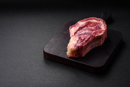 Fresh juicy raw beef striploin steak with salt and spices on a dark concrete backgroundの写真素材