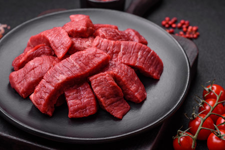 Fresh juicy raw beef slices with salt and spices on a dark concrete backgroundの写真素材